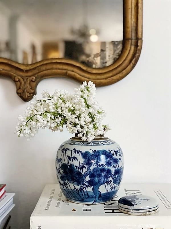 blue and white ginger jar with white flowers on top of books.