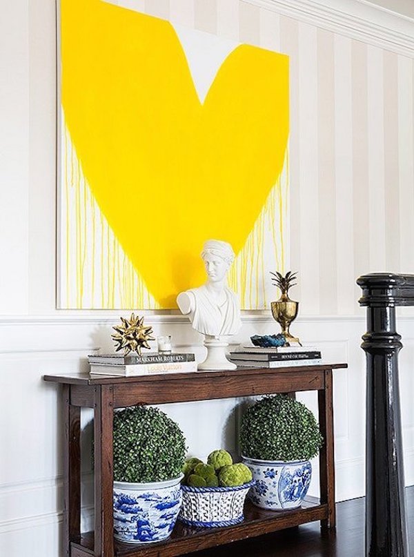 yellow drippy heart art in hanging above dark wood console.