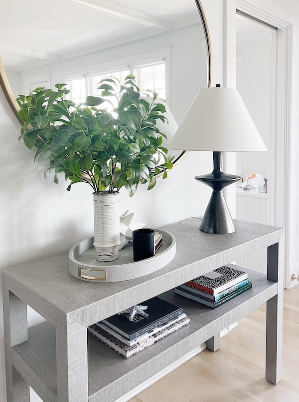 gray console with greenery in front of large round mirror.