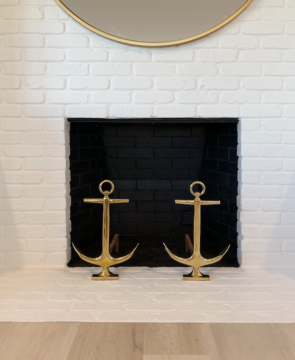 white painted brick fireplace surround with wood floors and brass anchor andirons.