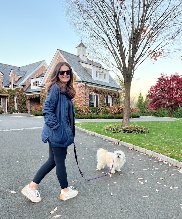 Woman walking dog in black leggings and sneakers.