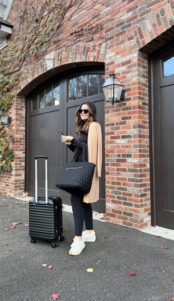 woman in a travel outfit outside with luggage.