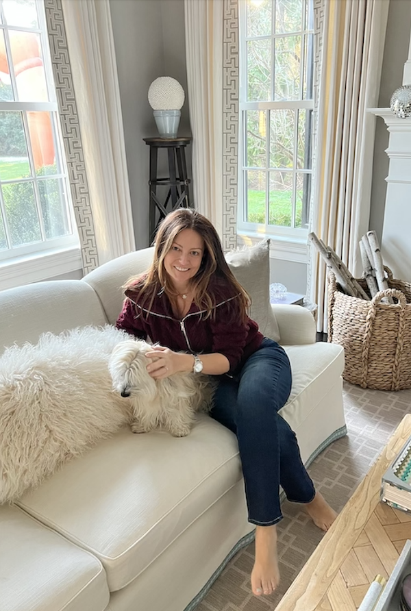 woman on sofa with small dog in wine colored sweater and jeans.