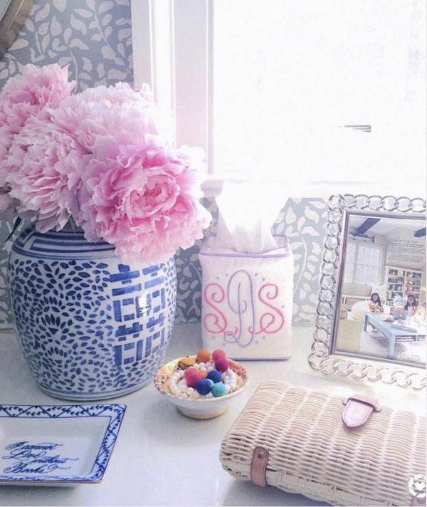 wicker clutch on counter next to blue and white vase of pink peonies.
