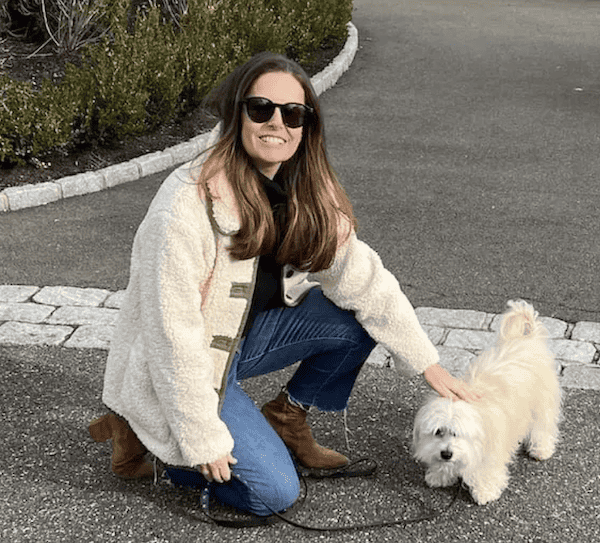 woman with small white dog wearing white fleece fall jacket.