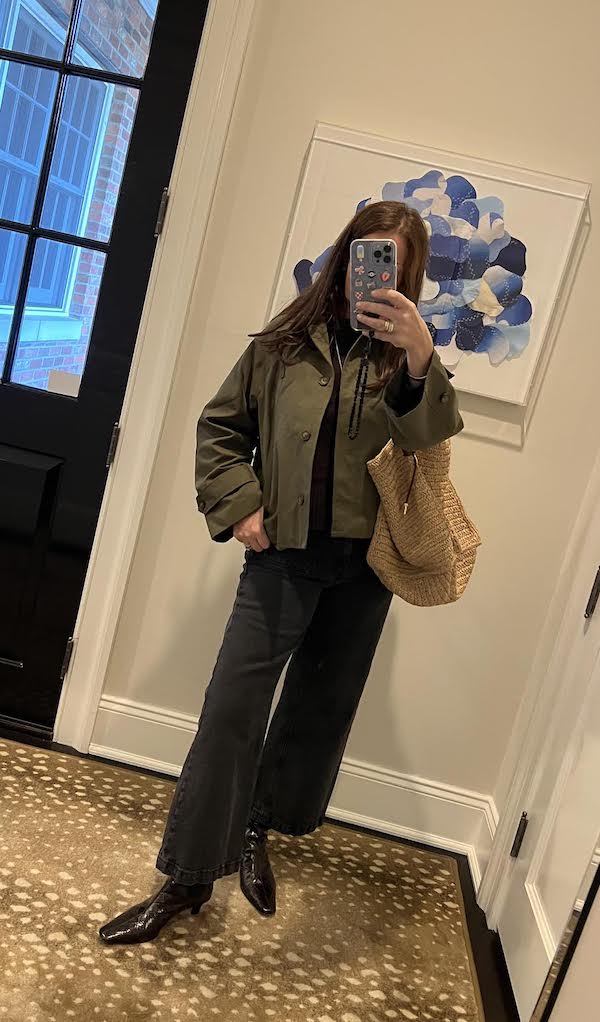 women in mirror with phone and raffia bag wearing trending ankle boots.