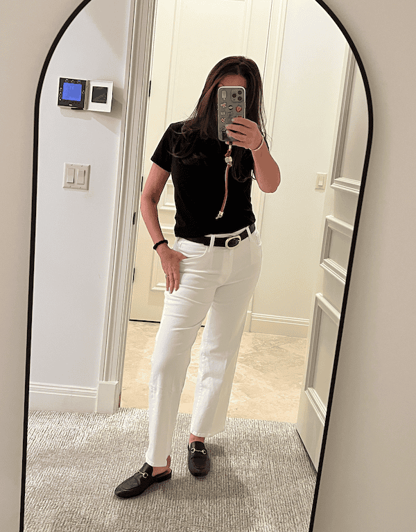 Woman over 50 wearing white pants with a black top, belt, and loafers showing a simple, chic outfit idea.