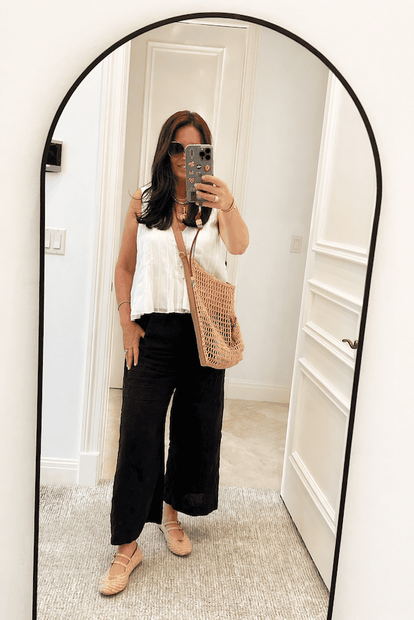 black linen pants outfit for women over 50 styled with a white sleeveless blouse, raffia bag and woven flats.