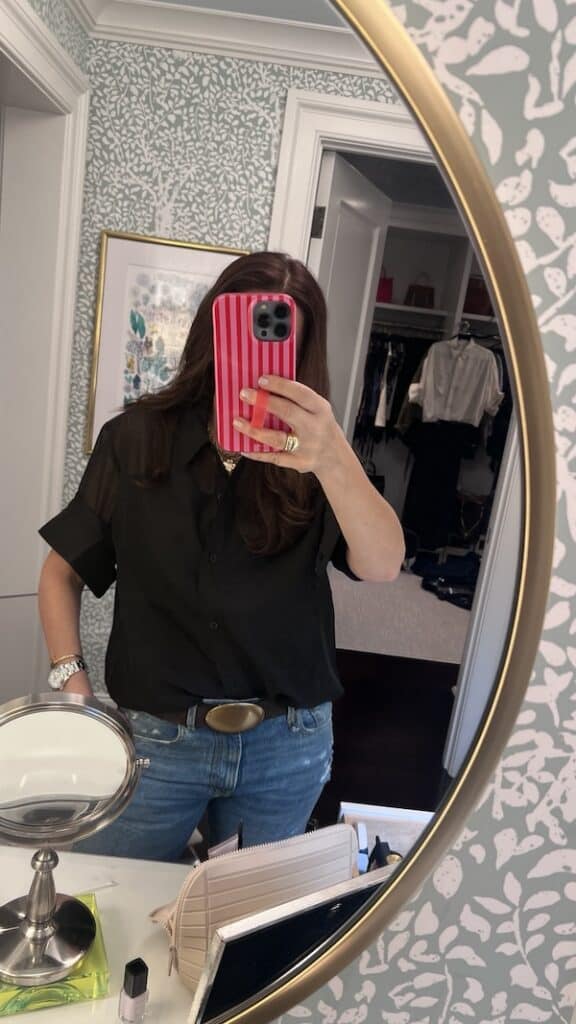 close up mirror selfie of woman in black button down shirt and jeans.